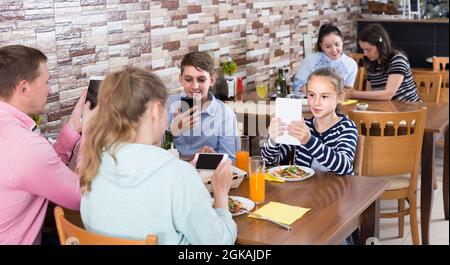Familie beschäftigt sich mit Telefon während des Mittagessens im Familiencafe Stockfoto