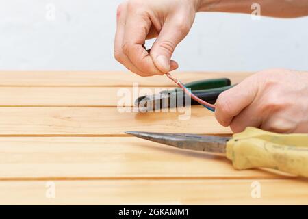Zwei Zangen und männliche Hände, die ein Elektrokabel über einem Holztisch halten Stockfoto