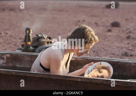 Obdachlose Frau, die in der Badewanne saß, den Spiegel ansah und ihr schmutziges Gesicht wusch, sie saß in der Wüste Stockfoto