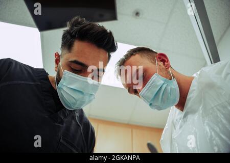 Zwei kaukasische Ärzte, die eine chirurgische Ausrüstung tragen und auf den Patienten herabblicken Stockfoto