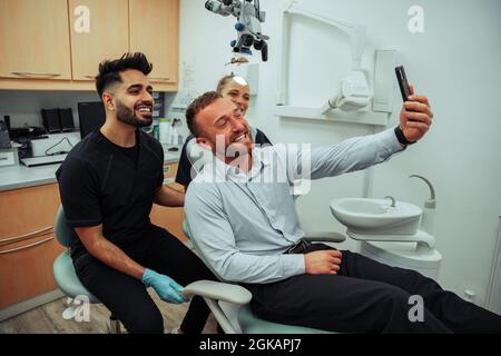 Kaukasischer männlicher Klient, der Selfie mit männlicher und weiblicher Krankenschwester nach erfolgreicher Zahnaufhellung einnahm Stockfoto