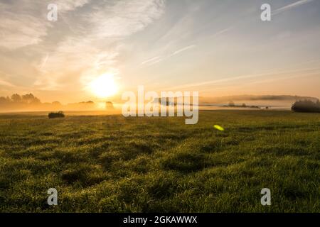 Schöner Sonnenuntergang in ländlicher Landschaft mit Sonnenstrahlen, die durch den Morgennebel scheinen Stockfoto