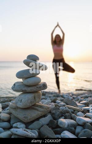 Balancing Cairn von Steinen auf dem Meeresstrand vor dem Hintergrund einer Frau aus Fokus Durchführung der vrikshasana Übung, Baum Pose Stockfoto