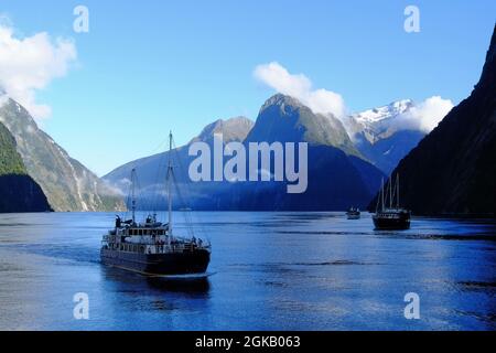 Berge, Schnee und Touristenkreuzfahrtschiffe an einem sonnigen Morgen im Milford Sound, Südinsel, Neuseeland, NZ Stockfoto