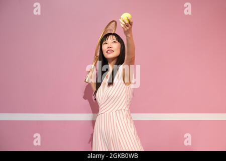 Junge asiatische Frau, die vor pastellrosa Hintergrund Tennis spielt. Stockfoto