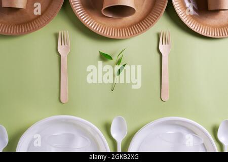 Ein Set aus Bambus-Holz-Geschirr mit einer Pflanze vor einem Set aus Kunststoff-Geschirr auf grünem Hintergrund. Umweltfreundliches Konzept. Draufsicht. Stockfoto