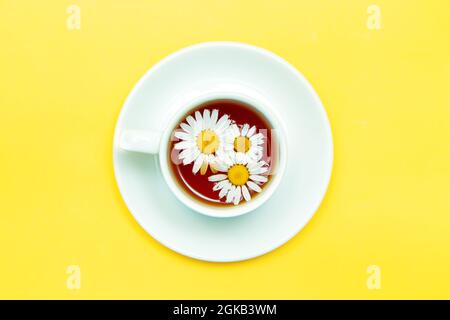 Kamillentee in einem weißen Becher auf gelbem Hintergrund. Mittel zur Entspannung, beruhigender Tee. Stockfoto