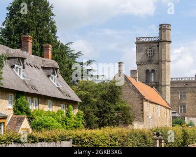 Viktorianischer Wasserturm, mit traditionellem Reethaus im Vordergrund, auf dem Gelände von Castle Ashby House, Northamptonshire, Großbritannien Stockfoto