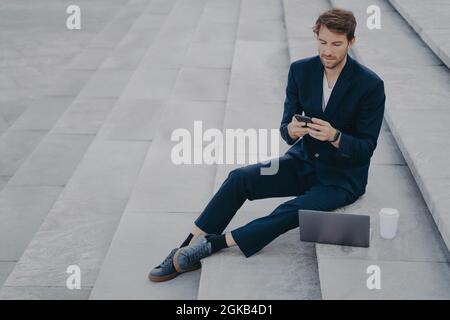 Ein leitender Angestellter verwendet ein Mobiltelefon zum Chatten von Arbeiten aus der Ferne macht Projekte über einen Laptop-Computer Stockfoto