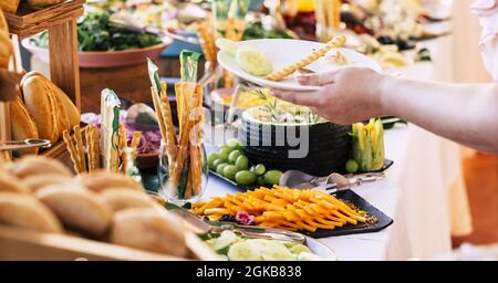 Unerkannte Person, die Essen auf dem Teller serviert, mit verschiedenen Brotsorten, die auf dem Tisch auf dem Buffet ausgestellt werden, im Luxusrestaurant. Menschliche Hand, die Essen serviert i Stockfoto