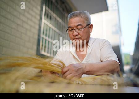 (210914) -- XINYU, 14. September 2021 (Xinhua) -- Li Nian'gen stellt Bambuswebprodukte in der Gemeinde Dongcun, Bezirk Fenyi, Stadt Xinyu in der ostchinesischen Provinz Jiangxi, her, 1. September 2021. Li Nian'gen, 62, ist die fünfte Generation der Bambuswebtechniken in der Gemeinde Dongcun. Li erwarb Bambuswebtechniken von seinem Onkel, als er gerade einmal neun Jahre alt war, und begann mit 15 Jahren, seinen Lebensunterhalt allein zu verdienen. Mehr als 20 seiner Lehrlinge entschieden sich Anfang der 1990er Jahre, in anderen Lebensbereichen außerhalb seiner Heimat eine Beschäftigung für besseres Einkommen zu suchen, aber Li beschloss, zu bleiben und sich an seine p zu halten Stockfoto