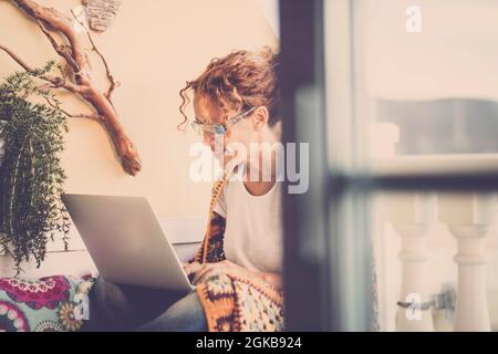Junge Frau, die einen Laptop benutzt und auf der Terrasse arbeitet. Zufrieden Frau arbeiten oder studieren auf Laptop auf der Terrasse des Hauses. Glückliche junge weibliche Browsi Stockfoto