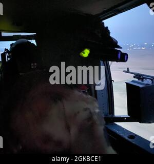 US Army Sgt. Gilberto Delossantos, Crewchef der Charlie Company, 1-137. Assault Helicopter Bataillon, 28th Expeditionary Combat Aviation Brigade, schaut auf die Seite eines UH-60 Black Hawk Hubschraubers, während sie nachts über das Einsatzgebiet des 28. ECAB im Nahen Osten fliegen. Stockfoto