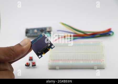 Junger Erfinder mit OLED-Display in der Hand, Arduino-Displaymodul mit Breadboard und Drähten auf einem Hintergrund, der kreative elektronische Projekte zeigt Stockfoto