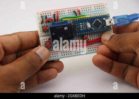 Erfinder, der sein kleines Grafikspiel zeigt, das von einem Satz von Knöpfen und einem Mikrocontroller gesteuert wird, der an einem Breadboard befestigt ist Stockfoto