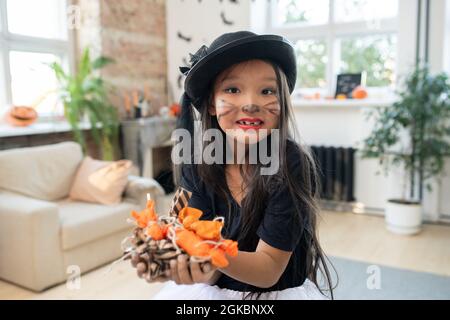 Nettes asiatisches Mädchen mit Haufen von Süßigkeiten in den Händen Blick auf Sie in der häuslichen Umgebung Stockfoto