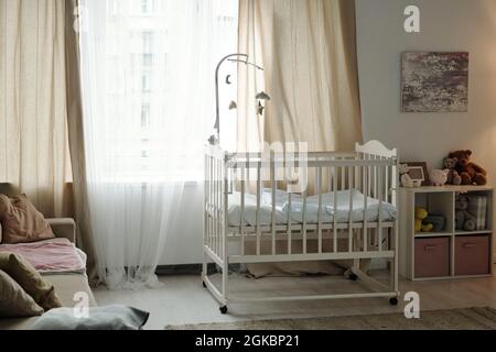 Teil des gemütlichen Schlafzimmers des neugeborenen Babys mit Kinderbett, das vor einem großen Fenster steht Stockfoto