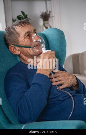 Ältere Senioren sitzen in einem Sessel mit einer Sauerstoffmaske in Quarantäne Stockfoto