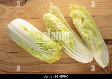 Eine ganze und zwei Hälften frischen Peking-Kohl auf einem Holztisch, Nahaufnahme, Draufsicht. Stockfoto