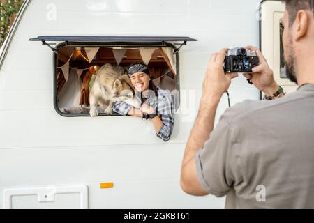 Niedliche weibliche und liebevolle Husky Hund posiert für Mann mit Fotokamera vor dem Travel House Stockfoto