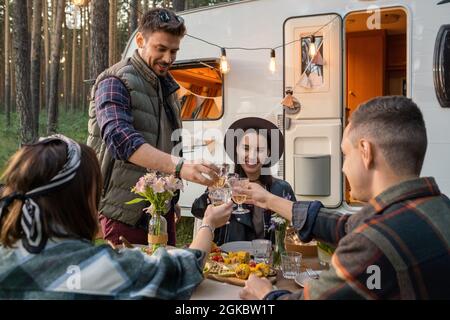 Glückliche Freunde klirren Gläser Wein über dem servierten Tisch, während sie das Abendessen im Haus auf Rädern genießen Stockfoto