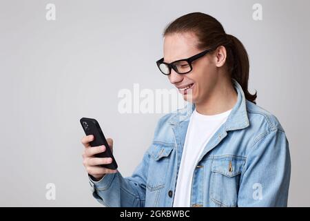 Junger Mann in Brille und Jeans-Jacke per Smartphone Stockfoto