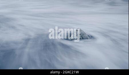 Langandauere Meereswellen und der Fels am Strand. Als die Wellen zum Meer zurücktraten, entstehen wunderschöne Linien zum isolierten Felsblock am san Stockfoto