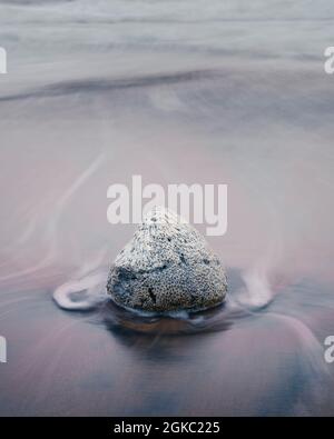 Korallenbrocken und die Strandwellen Langzeitaufnahme, seidig glattes Meerwasser, das am Felsen vorbei zurück ins Meer fegt. Stockfoto