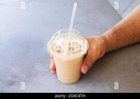 Mann hält Eiskaffee oder Latte in einer Plastikbecher zum Mitnehmen auf dem Steintisch des Straßencafés Stockfoto