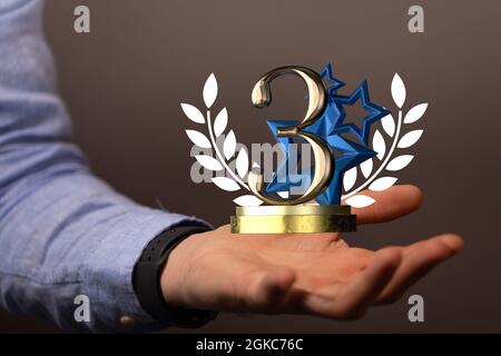 3D-Rendering eines goldenen Third-Place-Award-Konzepts mit blauen Sternen und einem Lorbeerkranz in der Hand Stockfoto