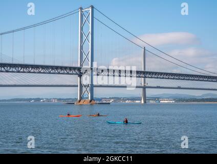 South Queensferry, Edinburgh, Schottland 7. September 2021 - drei Kajaks, die an einem sonnigen Tag bei klarem Himmel unter den Forth Road Bridges vorbeifahren. Stockfoto