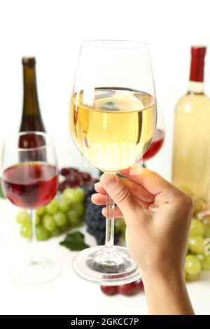 Weibliche Hand hält ein Glas Weißwein gegen verschiedene Weine Stockfoto