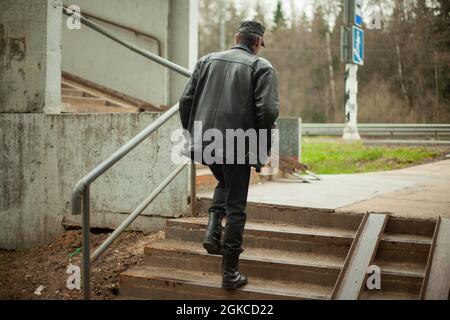 Der Mann steigt die Treppe hinauf. Eine Person geht die Stufen hinauf. Alte Fußgängerüberführung. Ort der Kreuzung der Straße. Ein Mann in schwarzer Lederkleidung. Leder j Stockfoto