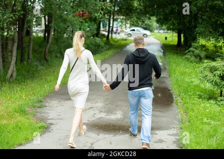 Ein Mann und ein Mädchen halten sich die Hände. Ein junges Paar geht durch die Stadt. Ein paar gehen die Straße runter. Junge Menschen lieben einander. Foto von der Rückseite. Stockfoto