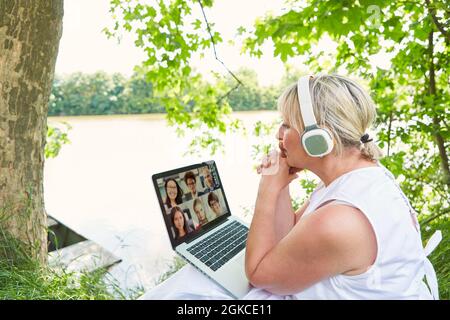 Geschäftsfrau bei Videokonferenz am Computer in grüner Natur am See im Sommer Stockfoto