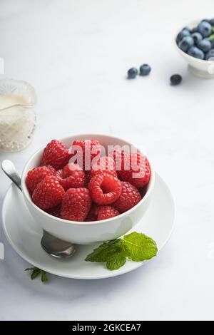 Schüssel mit frischen Himbeeren mit Heidelbeeren, Minze und Rahm. Stockfoto