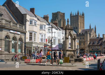 Wells Somerset, Blick im Sommer auf Menschen, die am historischen Market Place Cross und Fountain im Zentrum von Wells, Somerset, England, Großbritannien, vorbeigehen Stockfoto