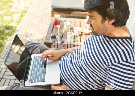Der junge Mann arbeitet als Freiberufler zu Hause auf der Terrasse am Laptop Stockfoto