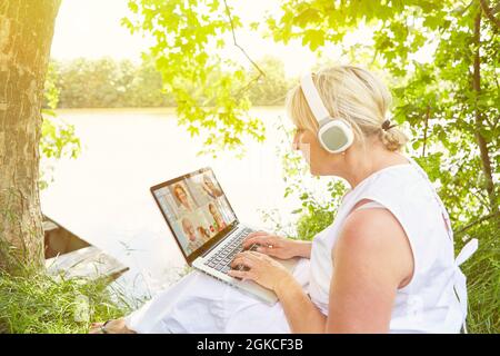 Eine Geschäftsfrau, die im Sommer bei einer Videokonferenz in der Natur mit einem Laptop unterwegs war Stockfoto