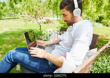 Junger Mann, der während einer Videokonferenz im grünen Garten als Freiberufler am Laptop-PC arbeitet Stockfoto