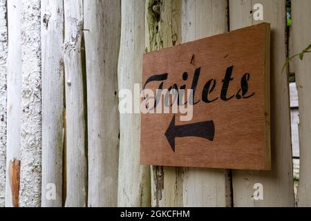 Ein rustikales Holzschild an einer Wand, das auf Toiletten zeigt Stockfoto