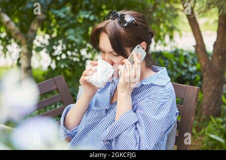 Eine Geschäftsfrau trinkt eine Tasse Kaffee und telefoniert mit dem Smartphone im Garten Stockfoto