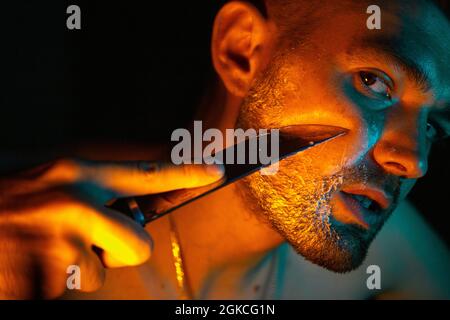 Ein Mann rasiert mit einem Messer in einem Neonlicht. Stockfoto