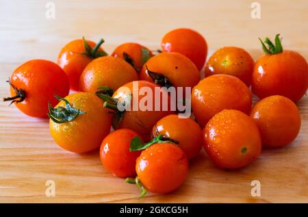 Frische Tumbling Tom Tomaten komplett mit ihren Stielen und kleinen Tropfen Wasser auf einem hölzernen Schneidebrett Stockfoto