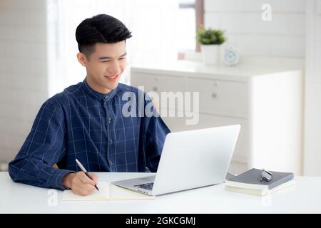 Junge asiatische Geschäftsmann schreiben auf Notebook für die Planung der Arbeit und mit Laptop-Computer auf dem Schreibtisch zu Hause, Notizen über Finanzen, männliche Studie und lernen Stockfoto