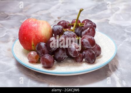 Ein Bund grüner Trauben und ein Apfel auf einem Teller mit grauem Hintergrund. Draufsicht. Stockfoto