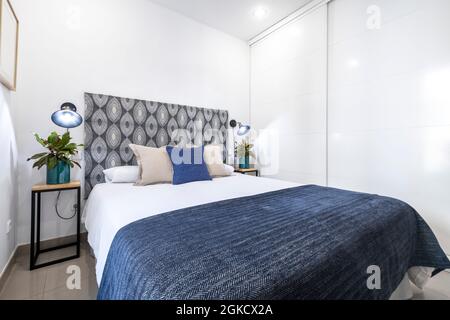 Doppelzimmer in Blau- und Weißtönen mit natürlichen Pflanzen auf den Beistelltischen und einem großen Einbauschrank an der Wand. Ferienwohnung apar Stockfoto