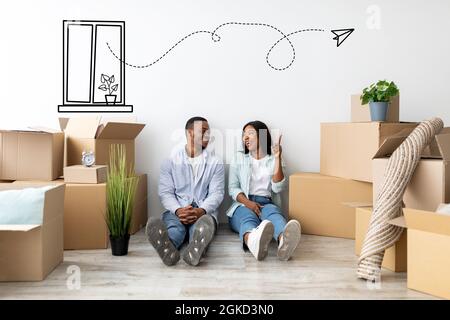 Immobilienkonzept. Junges afroamerikanisches Paar, das zwischen Kartons an der Wand sitzt und auf freien Raum zeigt Stockfoto