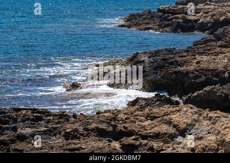 Felsige Küste und Wellen des Mittelmeers vor der Küste Zyperns in der Nähe der Stadt Paphos im Sommer bei gutem Wetter. Nasse Steine in der Nähe des mittelmeers Stockfoto