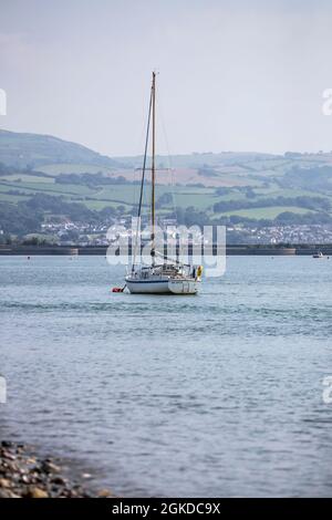 Eine Segelyacht namens „Solace“, die auf dem Fluss Conwy in der Mündung des Conwy in ruhigem Wasser mit gefurelten Segeln festgemacht ist. Stockfoto